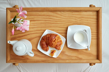 Top view of breakfast in bed with croissant, cup of milk and some flowers