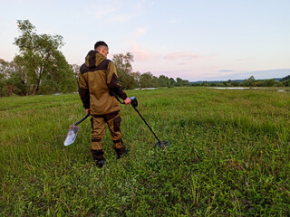 Metal search. A man is walking along a field with a metal detector and a shovel. Treasure hunt. A...