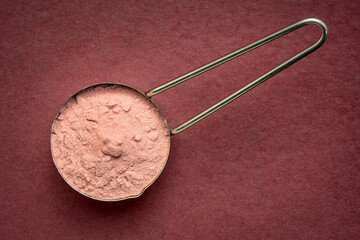 measuring scoop of pomegranate fruit powder - top view against handmade paper, superfood concept