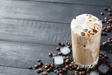 A glass of iced coffee with coffee beans and ice cubes on black wooden table. Selective focus. Copy space. Horizontal orientation
