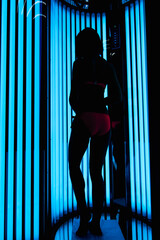 girl in the vertical Solarium. Silhouette on the background of ultraviolet lamps