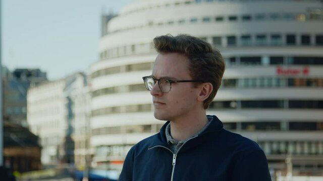 Modern caucasian with glasses looking up from phone commuting and navigating European downtown financial district pondering a 5g technological lifestyle