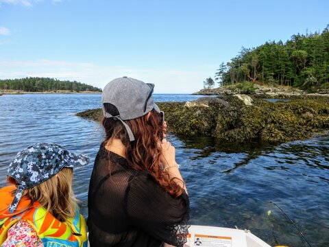 A mom and young daughter on a row boat taking a photo of a seal on a rock, while traveling in the Gulf islands, British Columbia, Canada