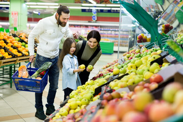 A young family with a daughter choose apples in the vegetable Department in the supermarket.