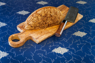 Half cut bread loaf on wooden olive wood board. Knife made from modern Damascus steel made by...