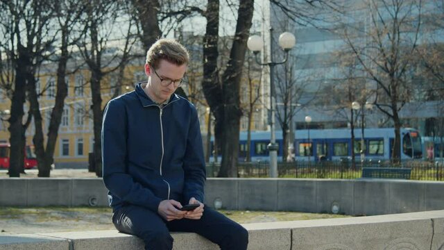 Tram going by in the background while a young man navigate his way by phone, concept of New ways of commuting with public transportation navigating in a digital age