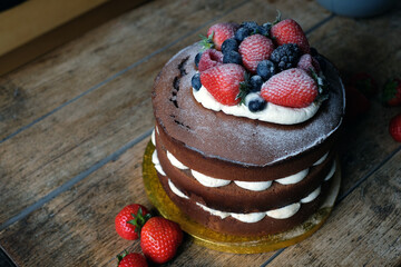 Delicious homemade cake with blueberries, raspberries, blackberries, strawberries and cream on the wooden background
