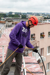 Worker fixing a rope equipment before descending from the roof. High-altitude works. Industrial alpinism.