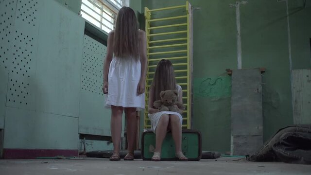 Two girls in the gym of an abandoned school, holding hands, facial hair. Mother and daughter or two sisters. Horror.Abandoned house. Mysticism.