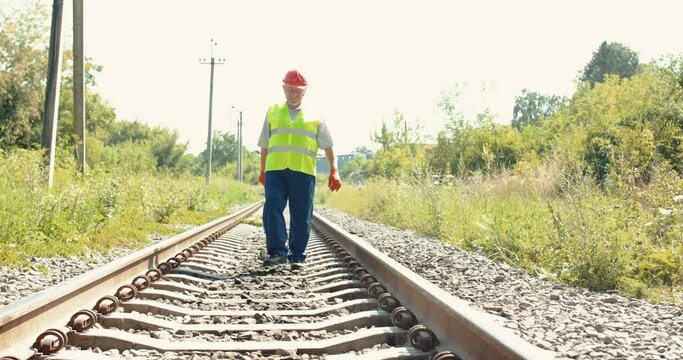 The railroader in uniform walking on railway with hammer and coming at camera