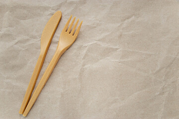 Biodegradable disposable cutlery: fork and knife on crumpled brown craft paper background. Copy space. Concept of zero waste, eco friendly. Selective focus