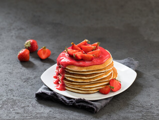 Pancakes with fresh strawberries and strawberry sauce on a plate on a linen napkin on a dark background