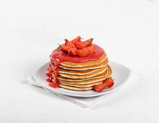Pancakes with fresh strawberries and strawberry sauce on a plate on a linen napkin on a white background