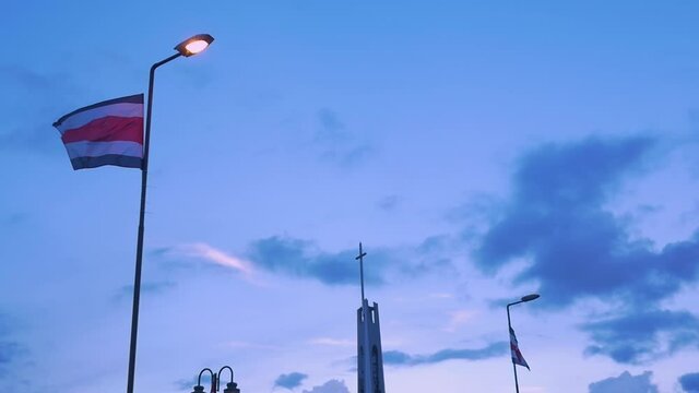 Bandera de Costa Rica en un parque publico frente a una iglesia cat&oacute;lica en una tarde de verano