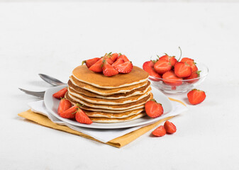 Pancakes with fresh strawberries on a plate on a linen napkin on a white background