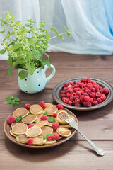 Pancake cereals on the fork. Red ripe fresh raspberries in a brown plate and a bunch of Melissa in a mug on the dark wooden table near the window. Delicious Breakfast