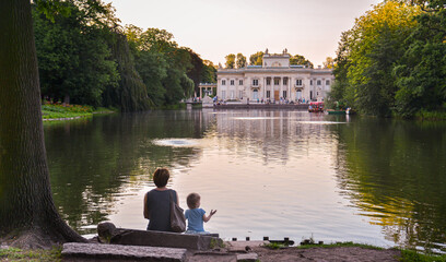 A woman and a little girl are sitting at the pond looking at the palace.
