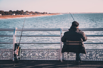 a fisherman on a chair holding a fishing rod fishing from a pier
