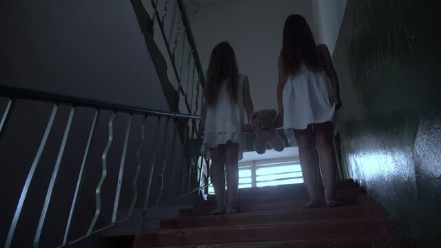 two girls with long black hair and a white dress walk down the stairs of an old abandoned school or house. the concept of maniac terror. Halloween.