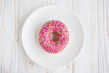 Colorful pink donut on a small white plate with white background. Fresh sweet colorful homemade vanilla donut on wooden background for birthday or party, top view, with free space for text