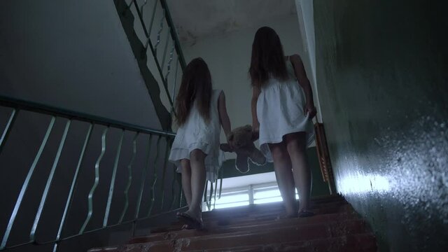 two girls with long black hair and a white dress walk down the stairs of an old abandoned school or house. the concept of maniac terror. Halloween.