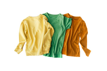 Three bright t-shirts in green, yellow and terracotta are beautifully laid out on a white background