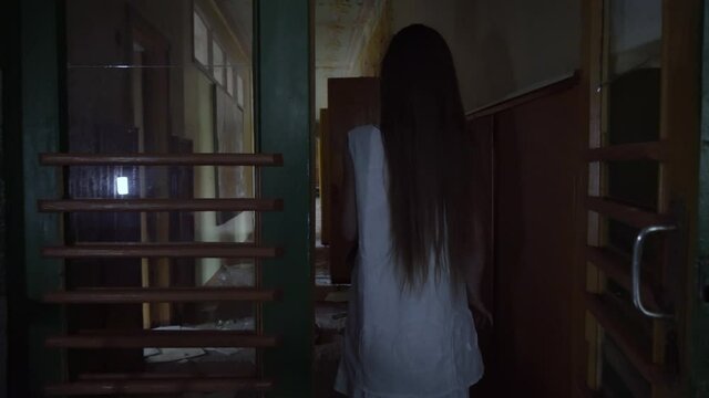 a girl with long black hair and a white dress is walking slowly in a dark corridor. The concept of a horror maniac. Halloween. she is holding a Teddy bear,