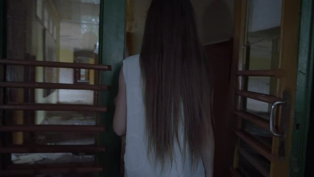 a girl with long black hair and a white dress is walking slowly in a dark corridor. The concept of a horror maniac. Halloween. she is holding a Teddy bear,