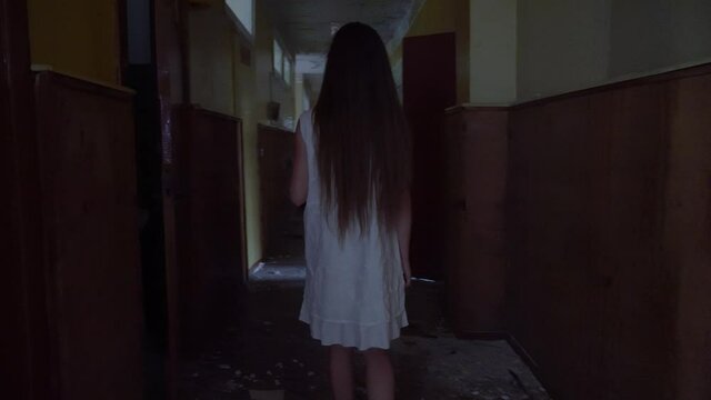 a girl with long black hair and a white dress is walking slowly in a dark corridor. The concept of a horror maniac. Halloween. she is holding a Teddy bear,