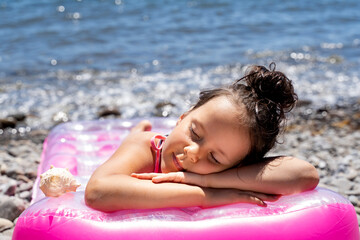 a beautiful little girl is sleeping on a bathing mattress by the sea.