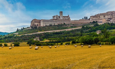 Fototapeta na wymiar Harvest time in the fields around Assissi, Umbria, Italy overlooked by the Basilica of Saint Francis in the summertime