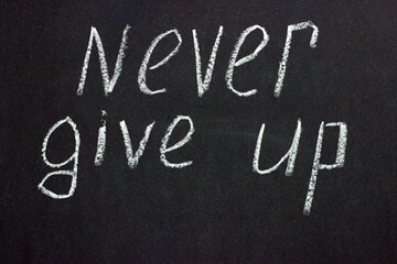 
Text on a dark board "never give up". Life-affirming and motivating phrase