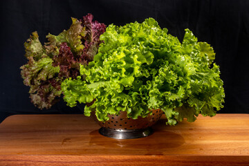 fresh green and red lettuce in a colander on wooden cutting board