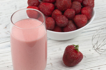 strawberry cocktail, blender and plate with strawberries on a white wooden background