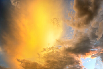 Dramatic sunset sky landscape with puffy clouds lit by orange setting sun and blue heavens.