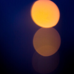Bright orange round blurred moon or traffic lights on dark blue violet bokeh background.