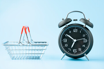Black vintage analog alarm clock and small shopping basket on blue background.