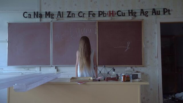 a girl with long black hair and a white dress walks slowly through the dark classroom of the school. The study of chemistry. Against the background of old test tubes and a blackboard.