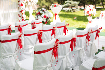 Wedding ceremony outdoors. White chairs with red ribbon.