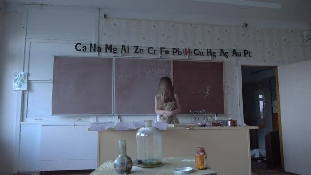 a girl with long black hair and a white dress walks slowly through the dark classroom of the school. The study of chemistry. Against the background of old test tubes and a blackboard.