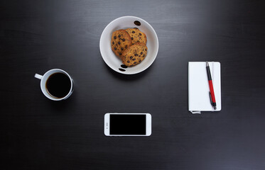 Obraz na płótnie Canvas Modern smartphone with blank screen lying flat on coffee table beside some brownies, coffee cup and a notebook