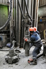 Two drilling crew workers dismantle the bottom of the drill string. Unscrewing the spiral calibrator. Working with a machine key. They are located on the rotary platform of the drilling rig.