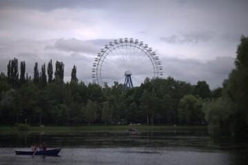 Panorama with a pond with boats, trees and a ferris wheel