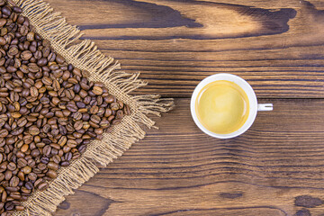 Arrow-shaped coffee beans indicate a cup of coffee. View from above. Cup of coffee and roasted coffee grains on a wooden background.