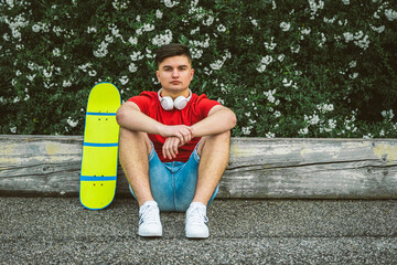 Fototapeta na wymiar Teen Boy is sitting resting with Longboard - Young adults outdoor skating - A young guy is sitting with a longboard - Portrait of beautiful boy skater