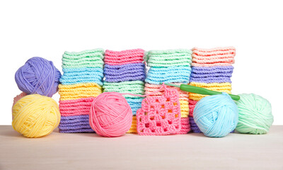 Piles of colorful hand crochet granny squares with balls of yarn piled behind on a light wood...