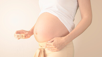 Pregnant young woman with pregnancy week number next to her belly. Photos of belly growth at 25...