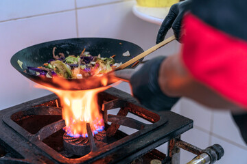 Chef making japonese food. Stir-fry soba noodles with beef and vegetables in wok pan on dark...