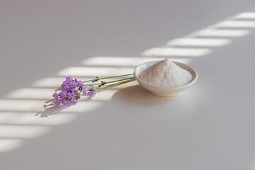 Selective focus to collagen powder in a white bowl and lavender sprigs on the table in morning shadow.