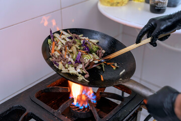 Chef making japonese food. Stir-fry soba noodles with beef and vegetables in wok pan on dark background
